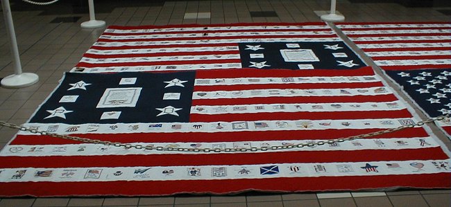 Two of the quilts on the floor, each with a framed dedication panel in its blue corner