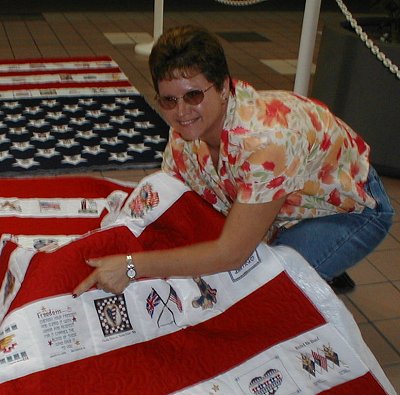 Sandra Hilliard kneeling beside a quilt and holding up the edge that carries her square