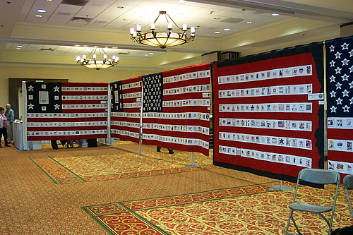 The memorial quilts hanging on frames in a carpeted exhibit hall under chandeliers