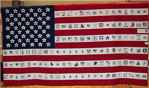 A flag-shaped memorial quilt with fifty stars and rows of cross-stitched squares in its stripes